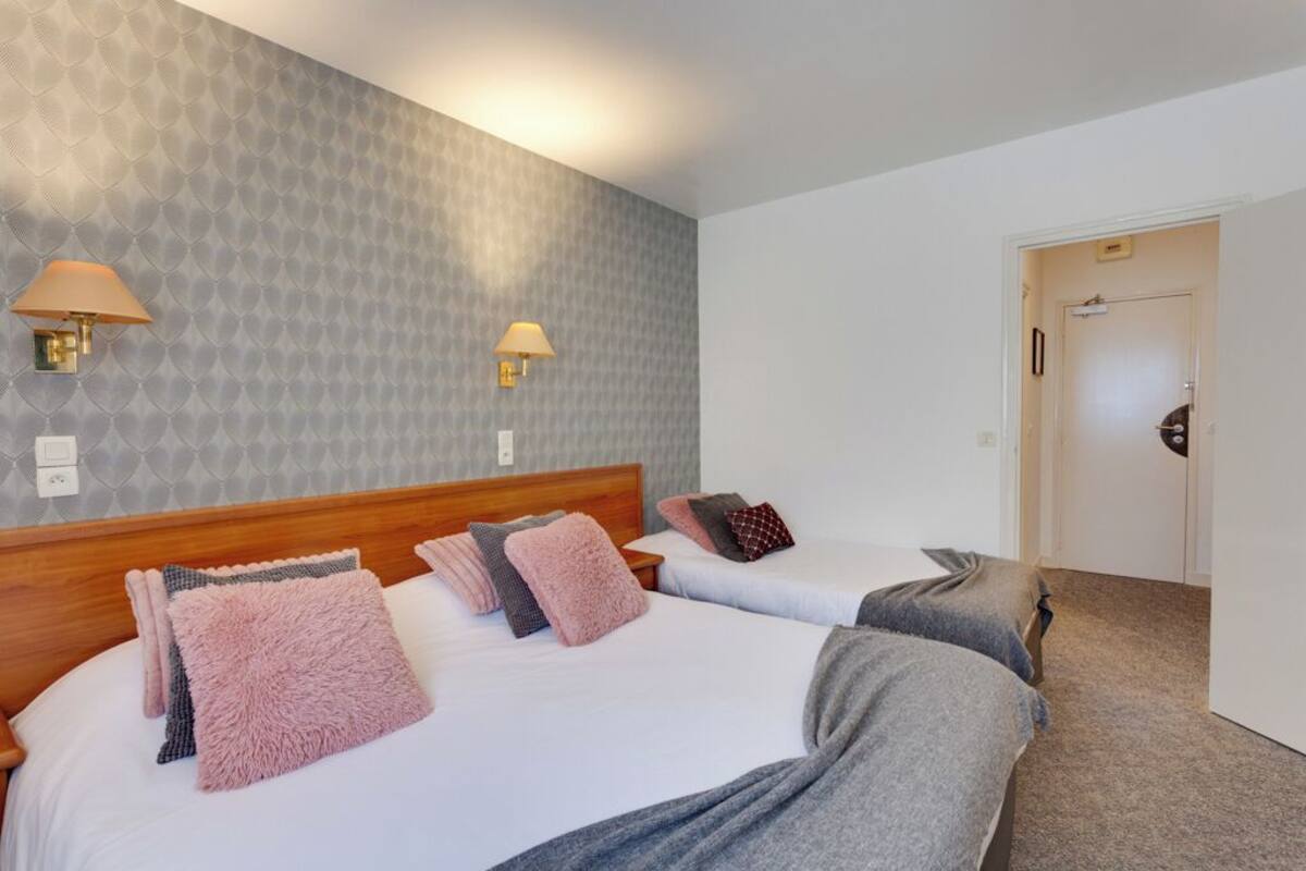 Une chambre d’hôtel avec deux lits, chacun doté d’une tête de lit en bois, et un mur décoré d’un motif. Deux lampes murales sont fixées de part et d’autre des lits.