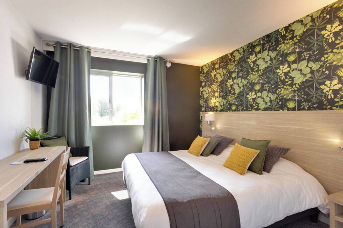 Une chambre d’hôtel avec un lit, un bureau, une chaise, une télévision et une fenêtre avec des rideaux.