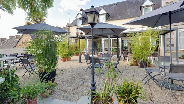 Un espace extérieur aménagé en terrasse, avec des tables et des chaises, entouré de plantes en pot et agrémenté de parasols.