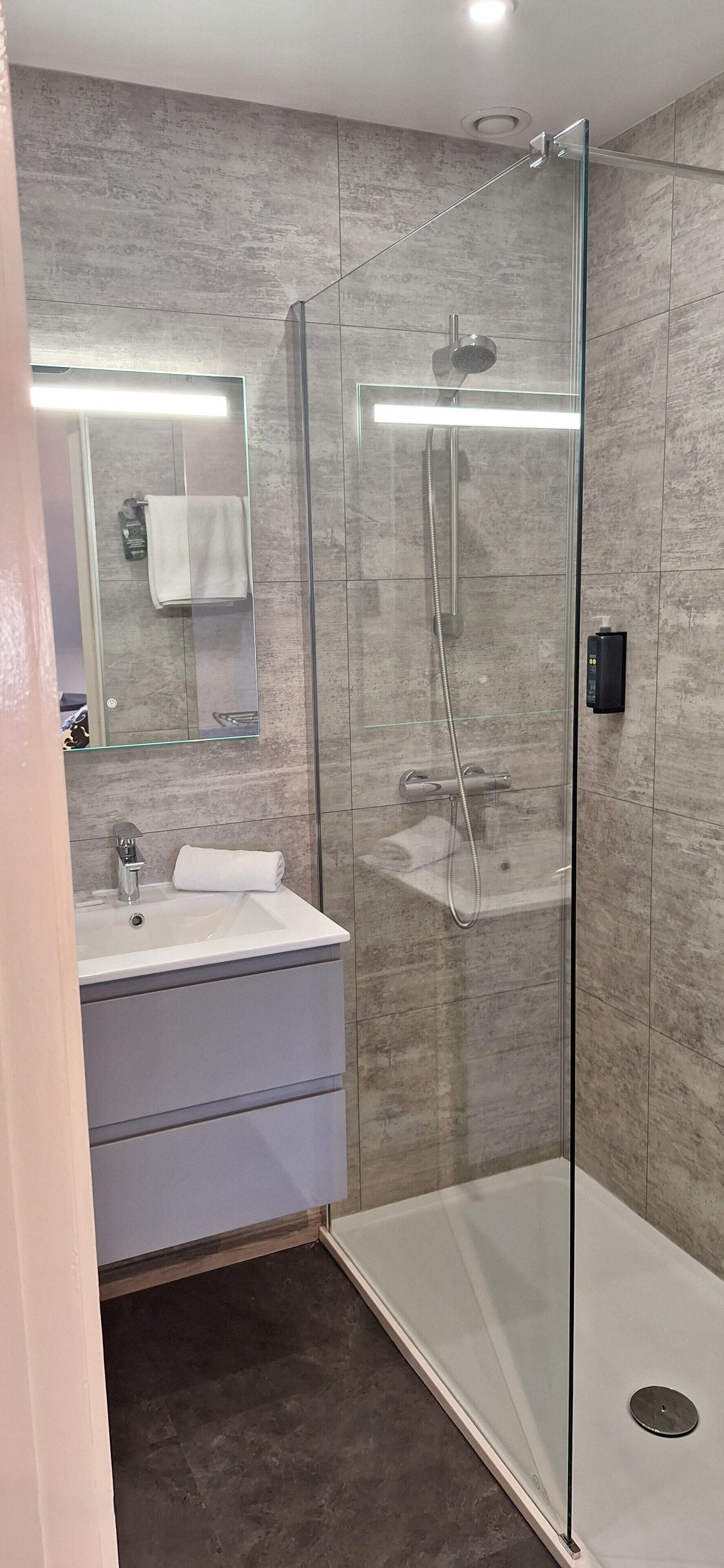 Une salle de bain moderne avec une douche à parois de verre, un lavabo avec une serviette et un miroir.