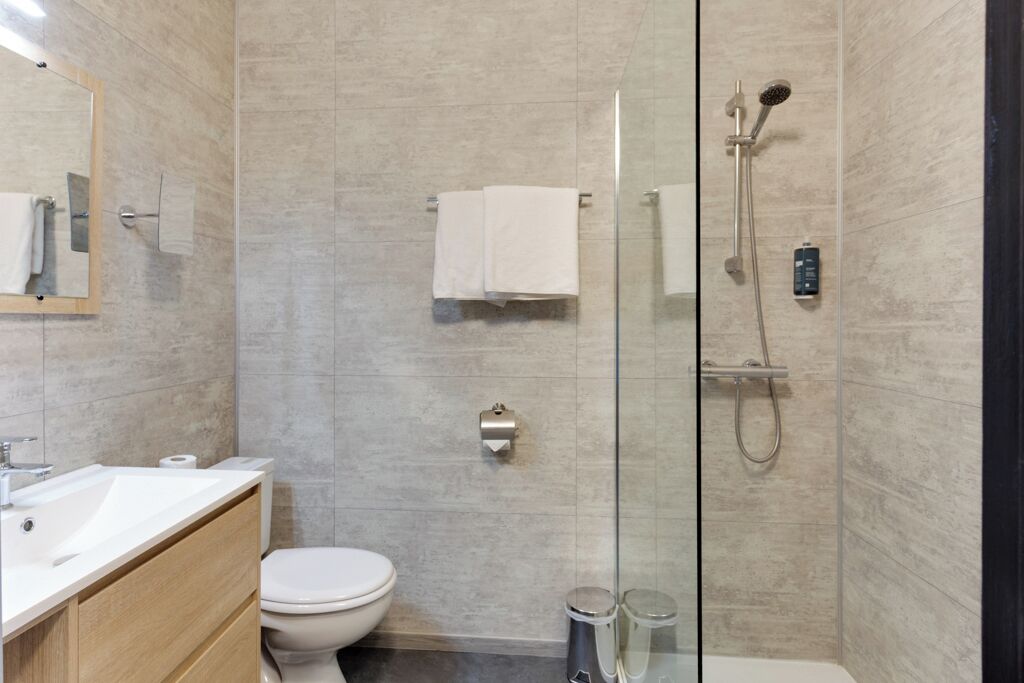 A modern bathroom with a glass-enclosed shower, a white toilet, a sink, and a mirror.