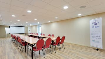 A conference room with long tables and red chairs, a whiteboard, and a projector screen.