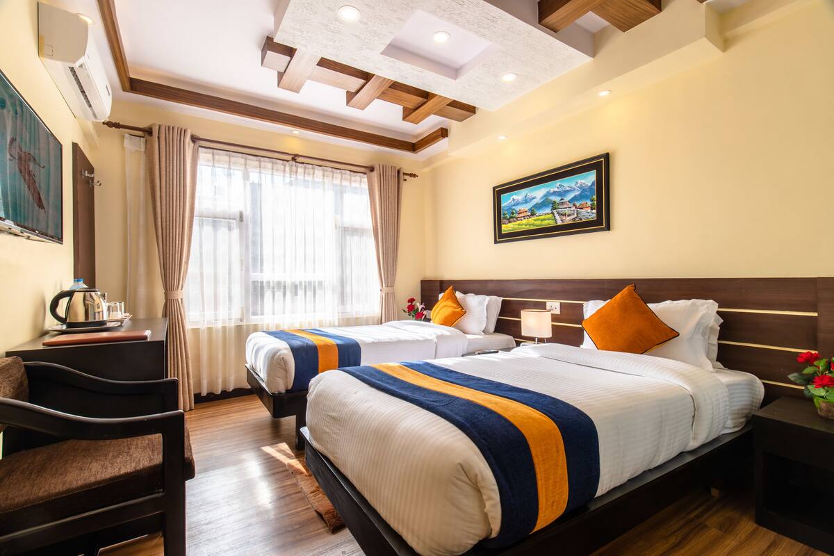 A hotel room with two beds, a desk, a chair, a nightstand, and a painting on the wall.