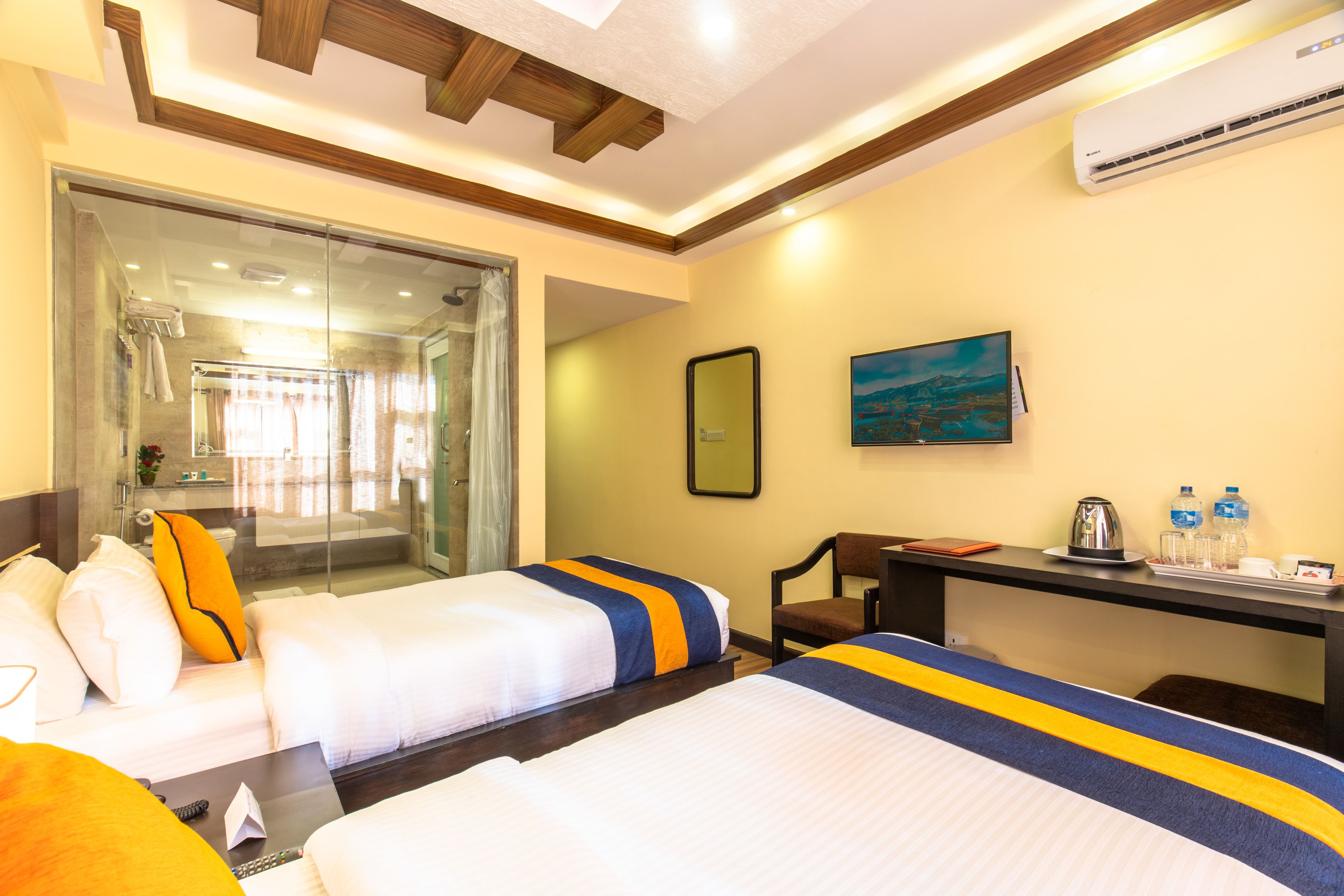 A hotel room with two beds, a desk, a chair, a shower area, and a painting on the wall.