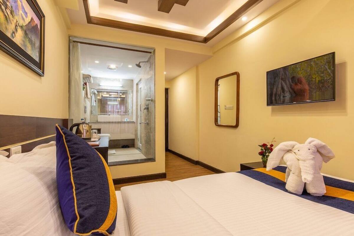 A hotel room with a bed, a mirror, a television, and a bathroom visible through an open door.