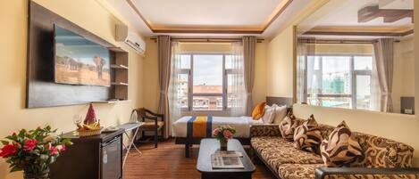Habitación de hotel con cama, sofá, televisor, escritorio y ventana con vistas a edificios.