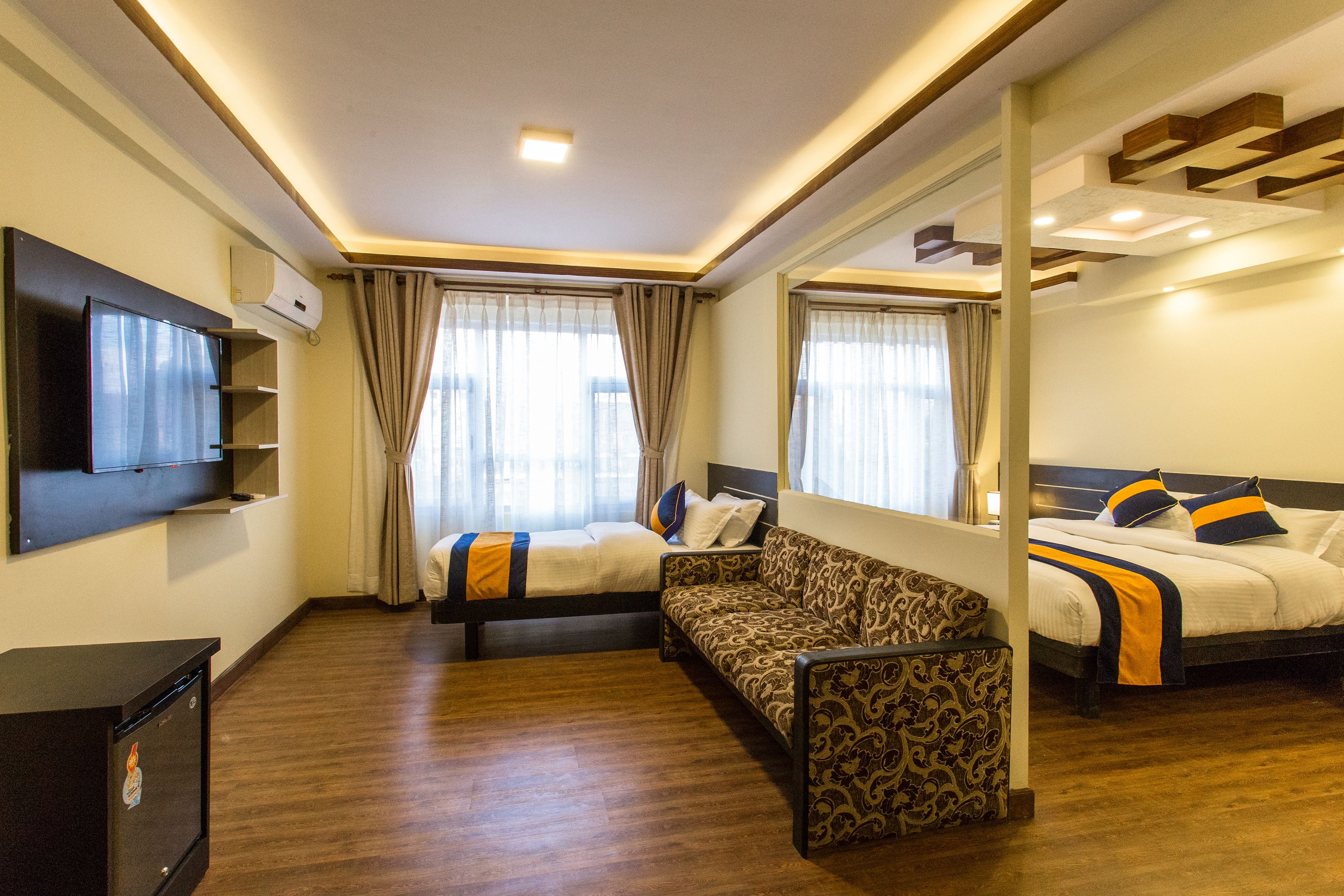 A hotel room with a sofa, two beds, a TV, and a minibar.