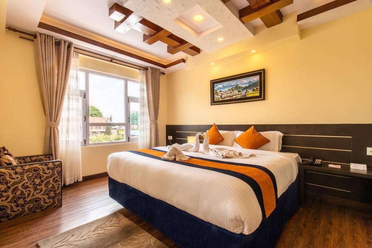 A hotel room with a large bed, a view of the city, and a painting on the wall.