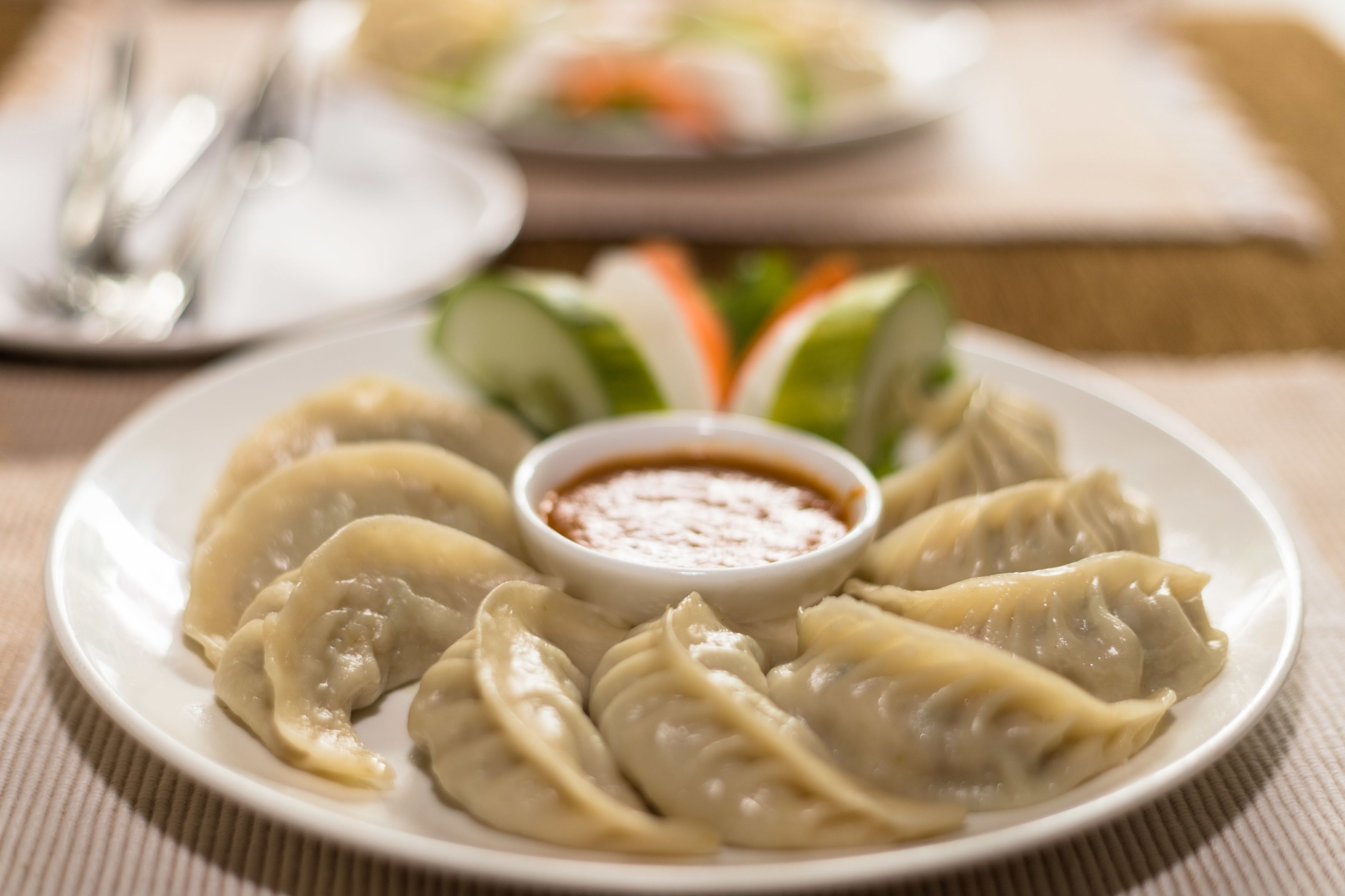 A plate of dumplings with a dipping sauce, accompanied by a salad and a plate of vegetables.