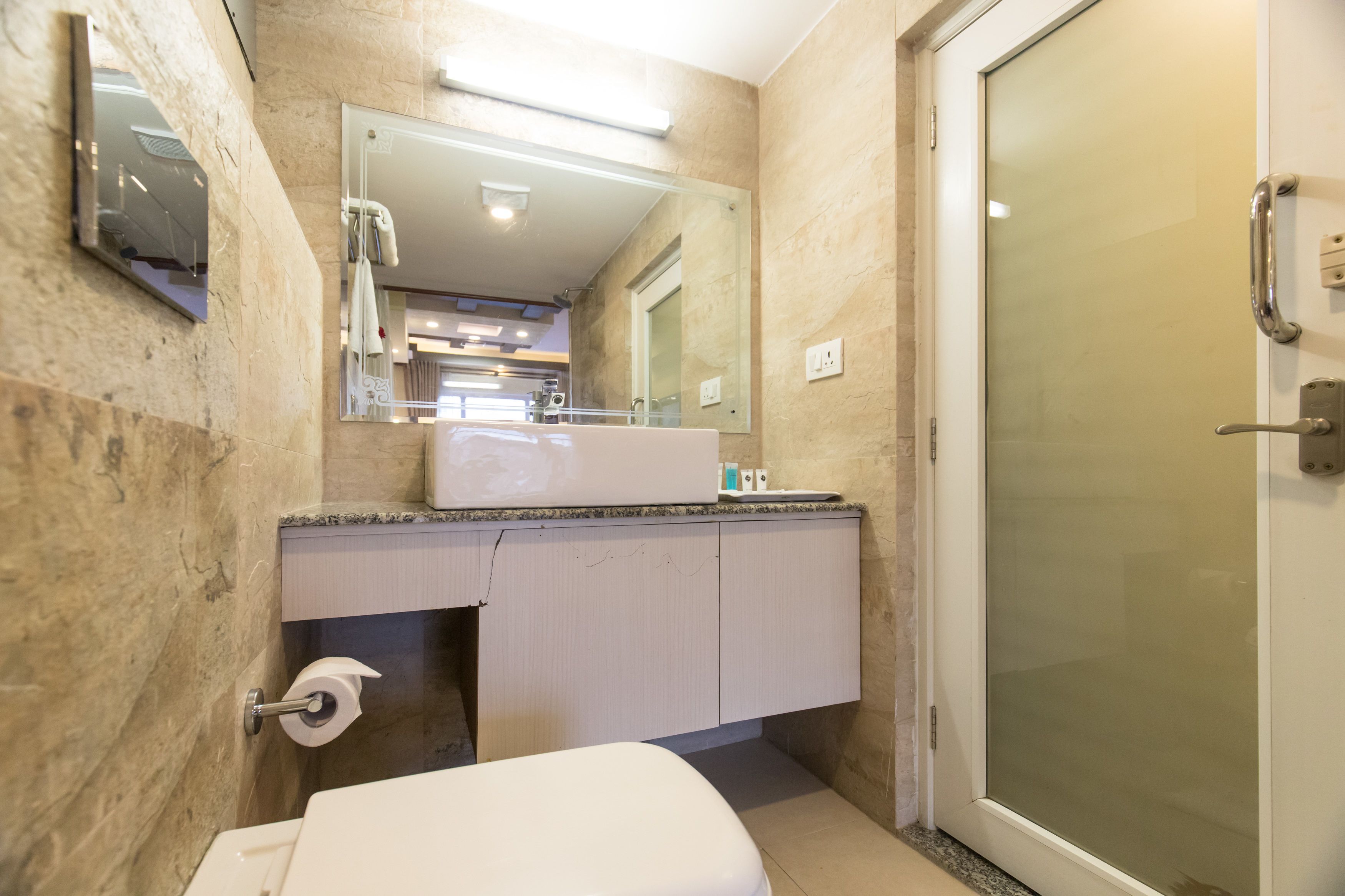 Un baño con inodoro, lavamanos, espejo y mampara de ducha de vidrio.