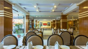 Une salle à manger d’hôtel avec plusieurs tables dressées pour les clients, un comptoir central et une vue sur l’espace extérieur.