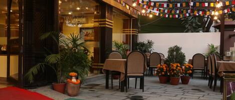 An outdoor seating area with tables and chairs, surrounded by potted plants and a decorative garland.