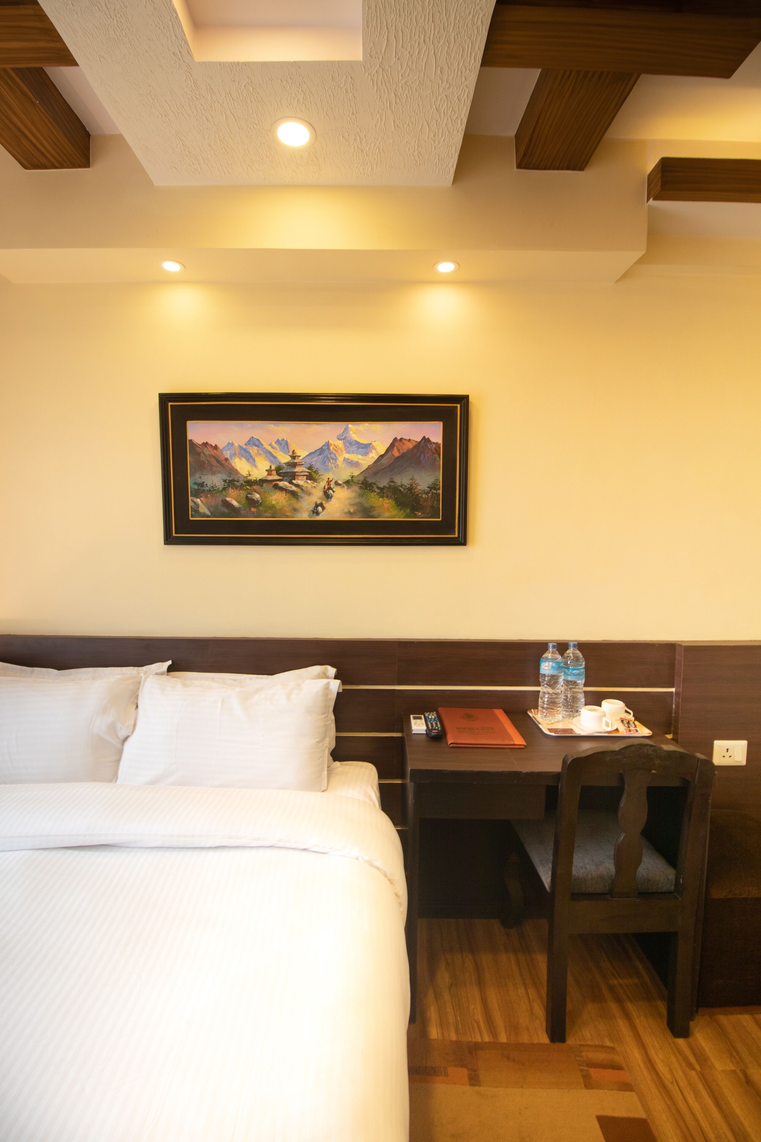 Une chambre d’hôtel comprenant un lit, un bureau, une chaise, un tableau encadré et une table avec une bouteille d’eau et une tasse.