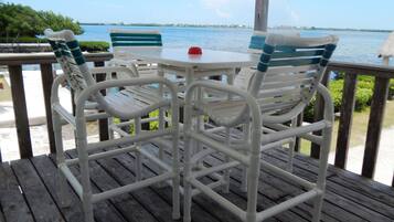 A wooden deck with white chairs and a table, overlooking a body of water.