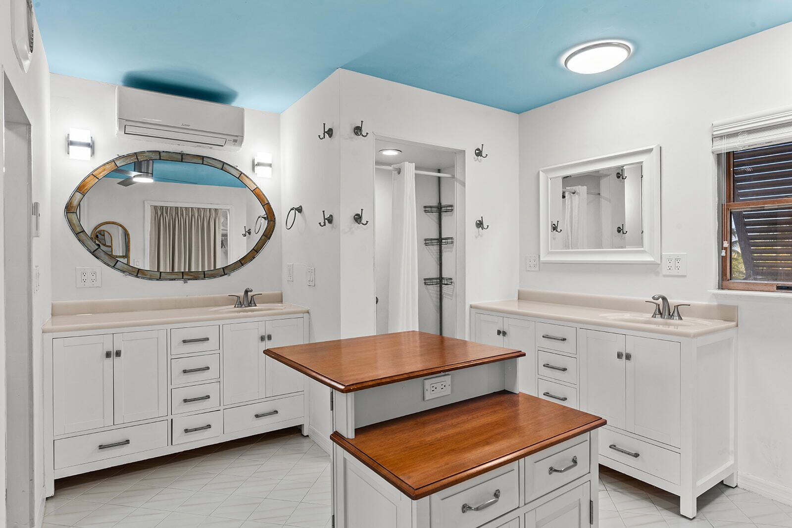 Une salle de bain avec des meubles blancs, un meuble-lavabo en bois, un grand miroir et un espace douche.