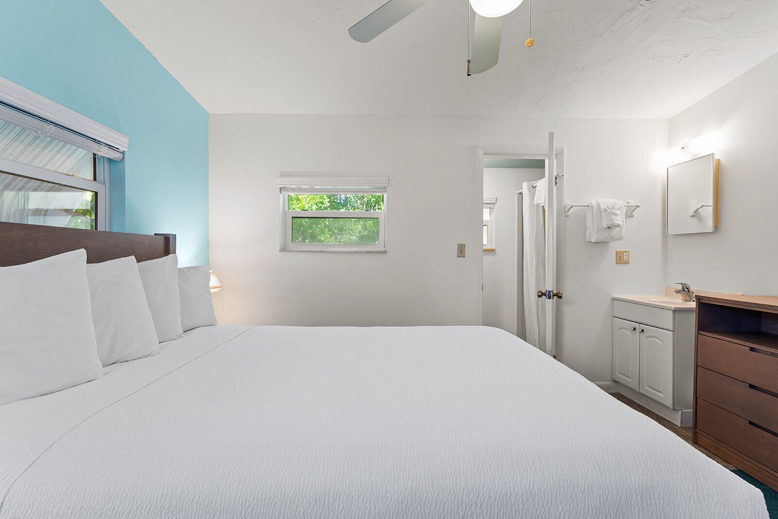 Une chambre à coucher avec un grand lit, une fenêtre, une porte et une salle de bain équipée d’un miroir et d’un lavabo.