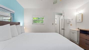 Une chambre à coucher avec un grand lit, une fenêtre, une porte et une salle de bain équipée d’un miroir et d’un lavabo.