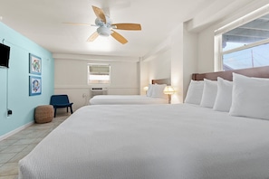 Relax in a spacious room with two comfortable beds, a ceiling fan, and a window offering a view of the outside.