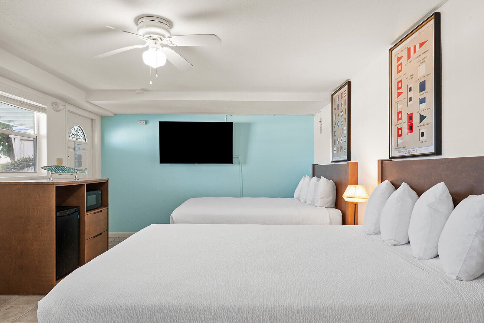 A hotel room with a bed, a desk, a television, and a ceiling fan.