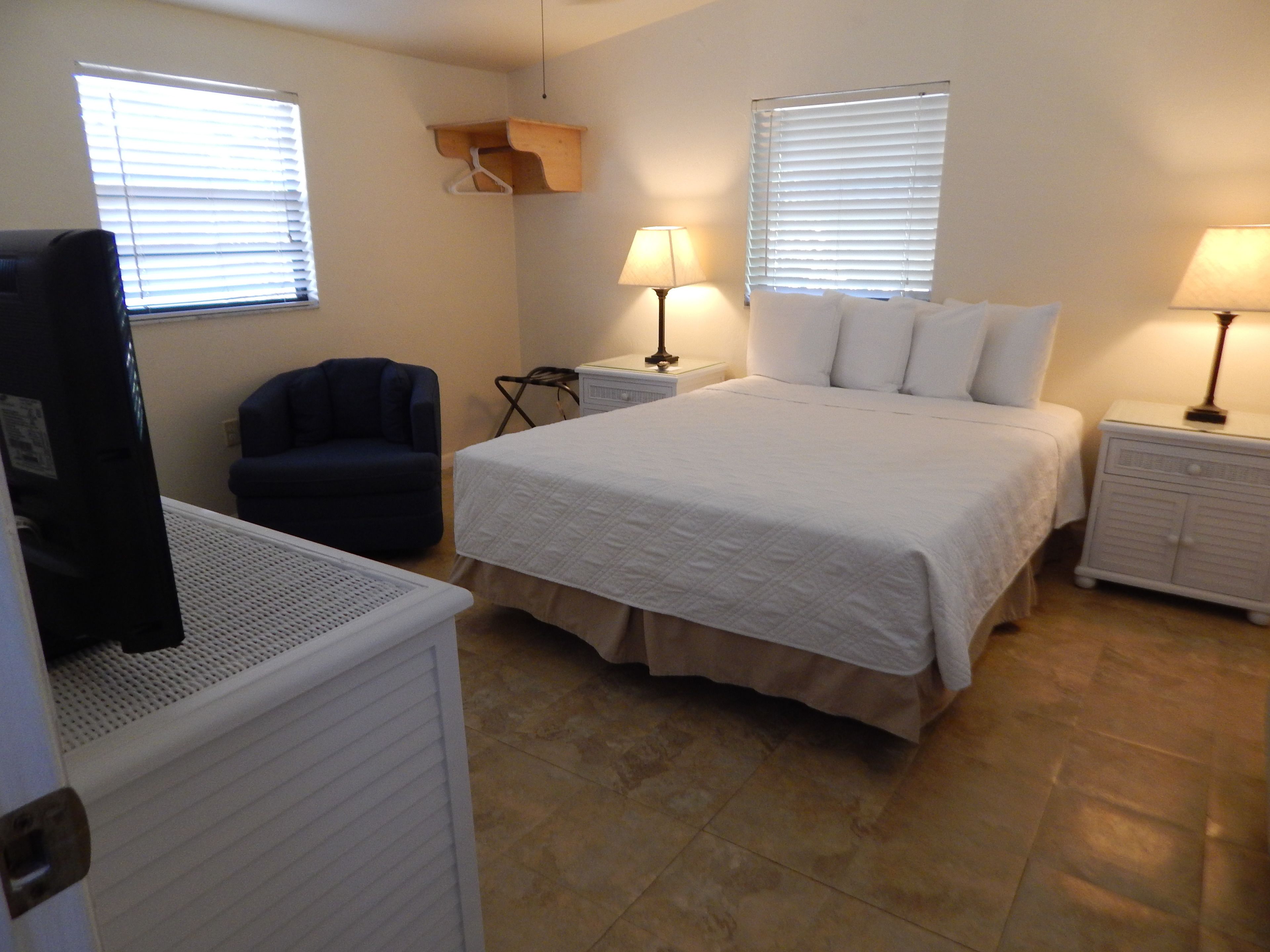A bedroom with a bed, two bedside tables with lamps, a chair, and a TV.