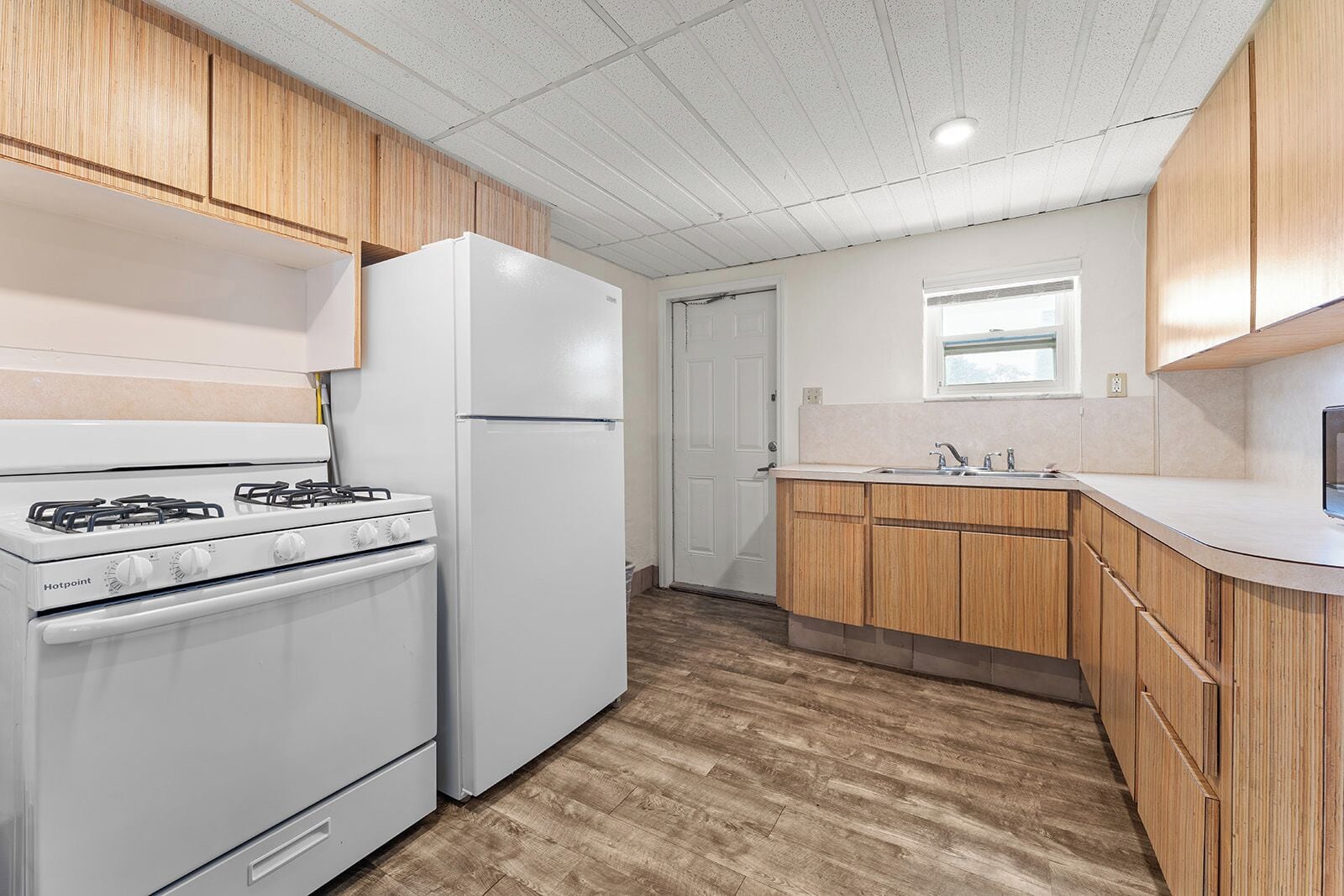 A compact kitchen with white appliances, wooden cabinets, and a window above the sink.
