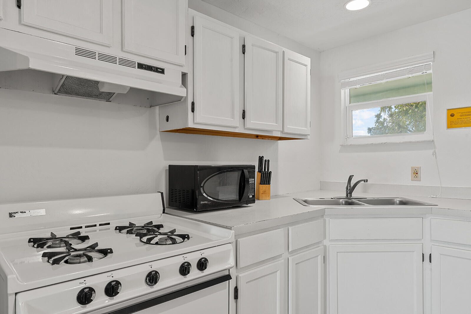 A kitchen with white cabinets, a stove, a microwave, and a sink.