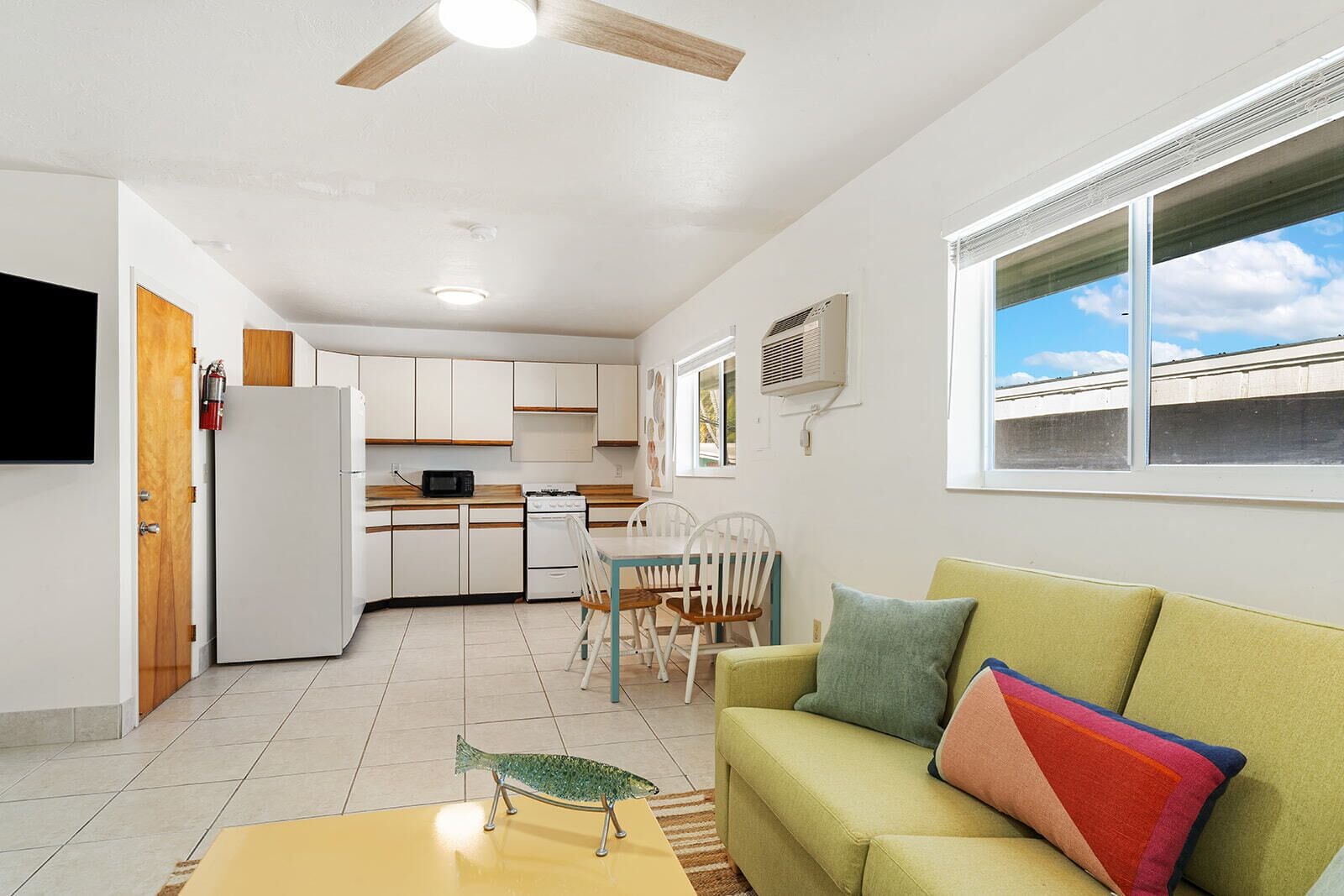 Ett kompakt bostadsutrymme med ett litet kök, en matplats och en soffa med färgglada kuddar.