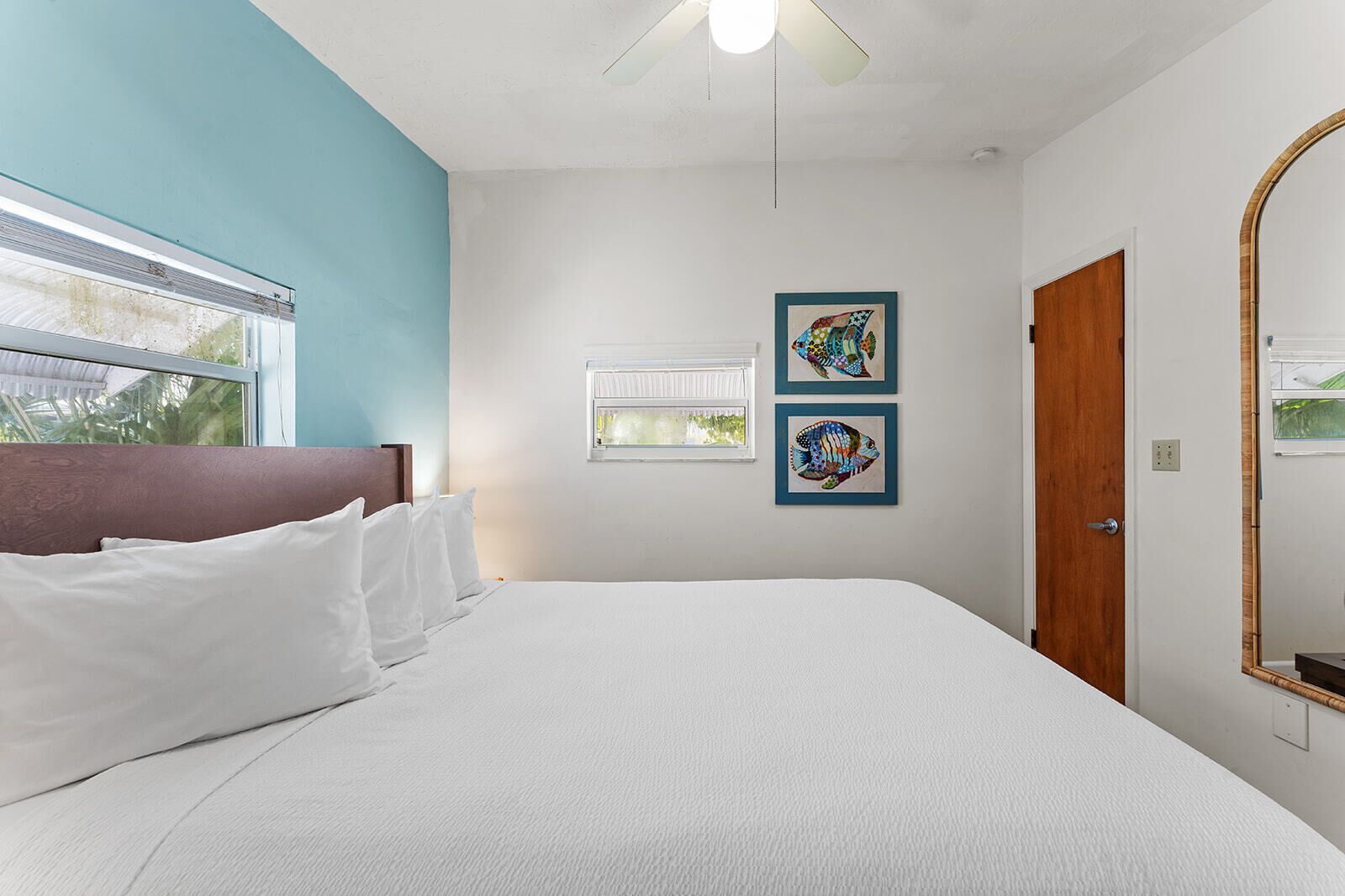 A bedroom with a bed, a window, a ceiling fan, and two framed pictures on the wall.