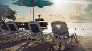 Beach chairs and a blue umbrella on a sandy shore with a calm body of water and a palm tree in the background. - Parmer's Resort (Summerland Key)