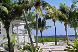 A white building with a covered patio area, surrounded by palm trees and a view of the ocean.