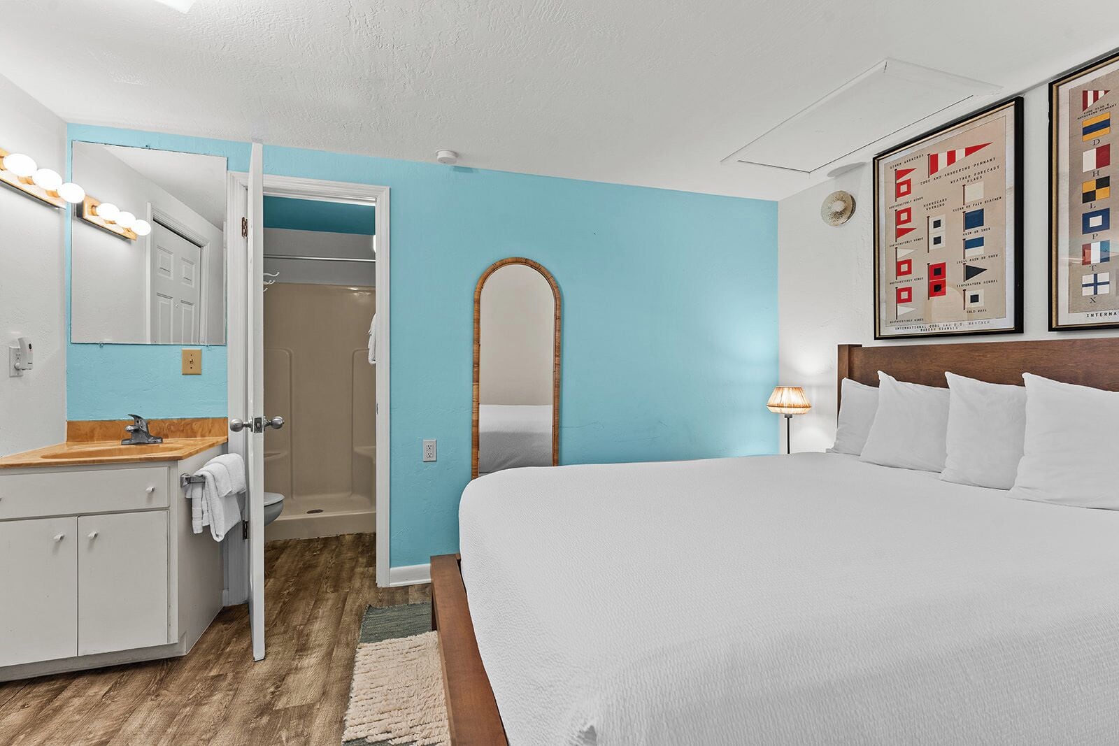 A hotel room with a bed, a bathroom with a shower, a vanity with a mirror, and a wall with framed pictures.