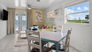 Un comedor con una mesa, sillas, ventilador de techo, televisor y ventana con vistas al exterior.