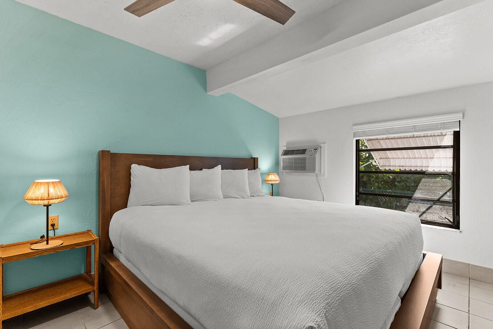 A bedroom with a bed, nightstands, and a window with an air conditioning unit.