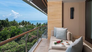 Uma varanda com vista para o oceano, um sofá com almofadas e um tabuleiro com frutas e chávenas.