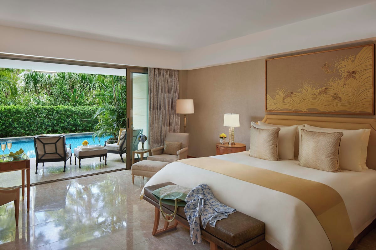 Habitación de hotel con una cama grande, vista a una piscina y un área de comedor con sillas y una mesa.