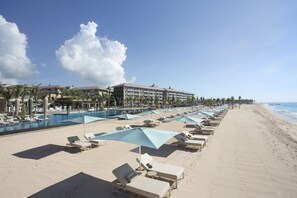 A beach resort with sun loungers, umbrellas, and a pool adjacent to the ocean.
