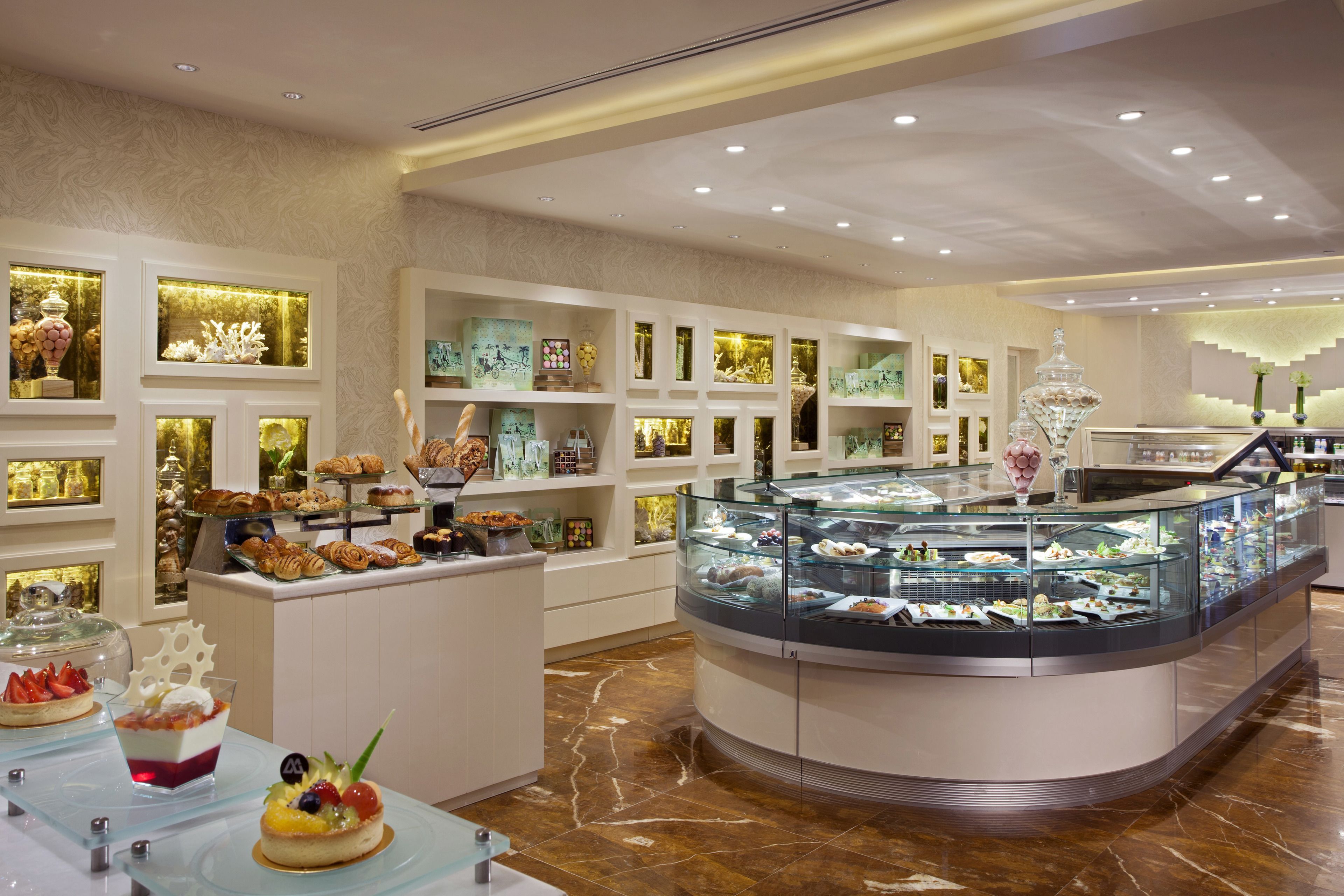 Un présentoir de desserts proposant une variété de pâtisseries et de douceurs, installé dans une pièce bien éclairée, au sol en marbre, avec des meubles blancs et des vitrines en verre.