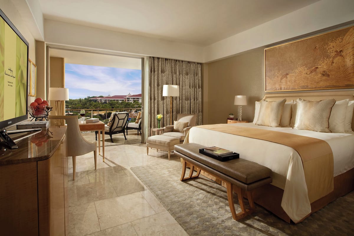 Habitación de hotel con una cama grande, un escritorio con computadora, una silla, una mesita con un jarrón y vistas al exterior.