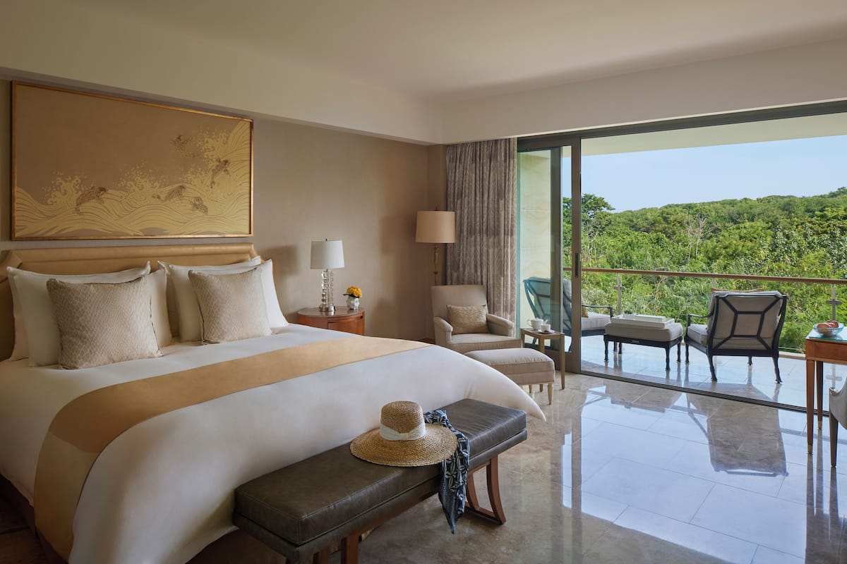 Habitación de hotel con una cama grande, un banco, una silla, una mesa y vistas al exterior.