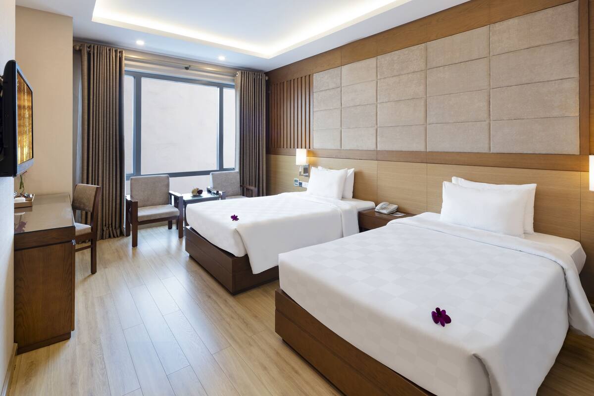 Une chambre d’hôtel avec deux lits, un bureau, une chaise et une grande fenêtre.