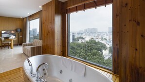 A modern bathroom with a freestanding bathtub, wooden flooring, and large windows offering a city view.