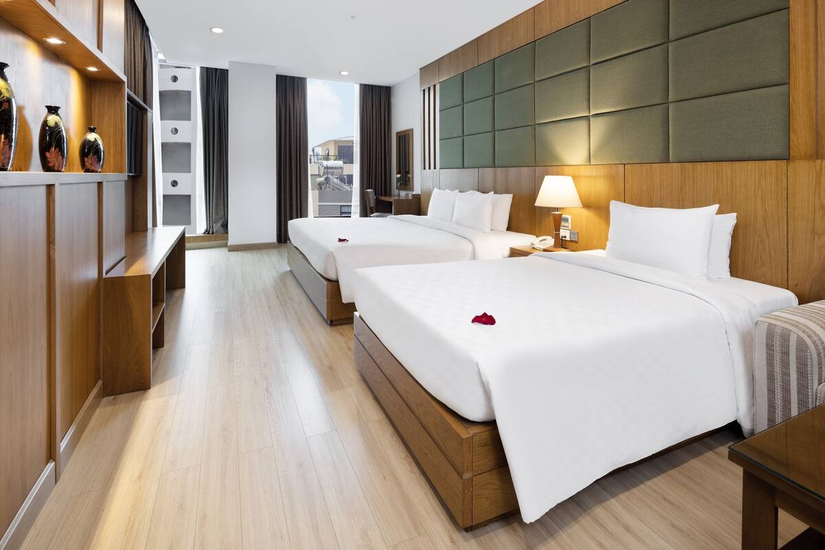 Une chambre d’hôtel avec deux lits, une tête de lit en bois, un bureau et une vue sur la ville.