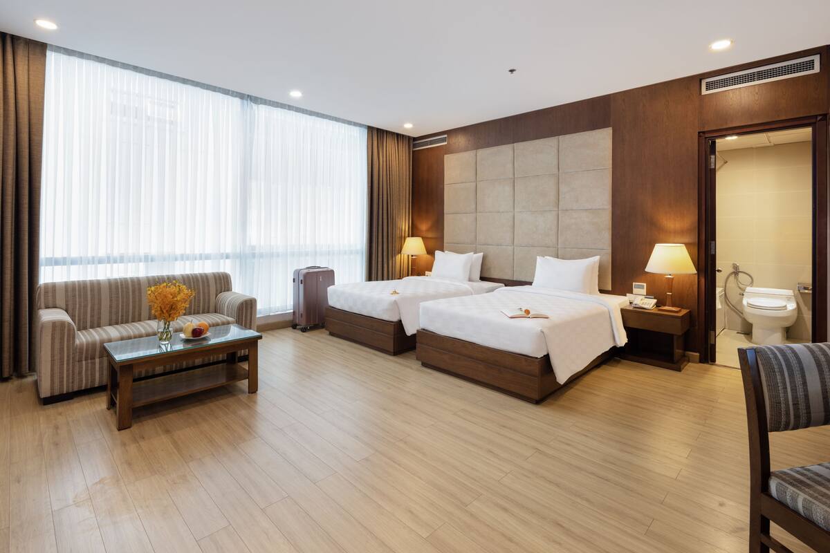 Une chambre d’hôtel avec deux lits, un canapé, une table basse et une salle de bain visible à travers une porte ouverte.
