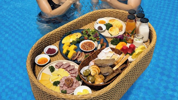 A couple in a pool with a floating basket of food and drinks.