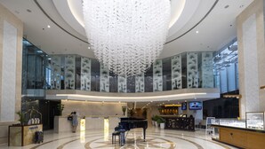 A spacious lobby with a large chandelier, a reception desk, and a piano.