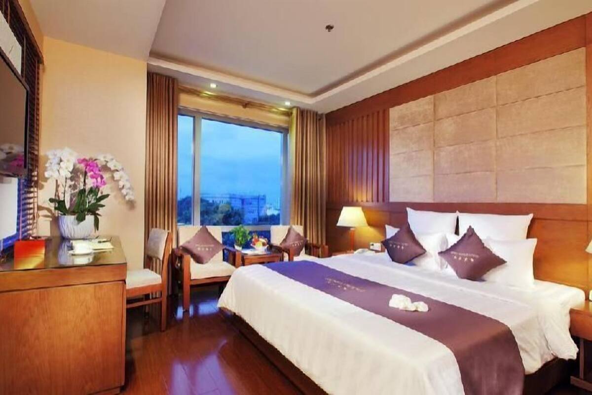 Une chambre d’hôtel avec un grand lit, un bureau, une chaise, une lampe et une vue sur le paysage urbain.