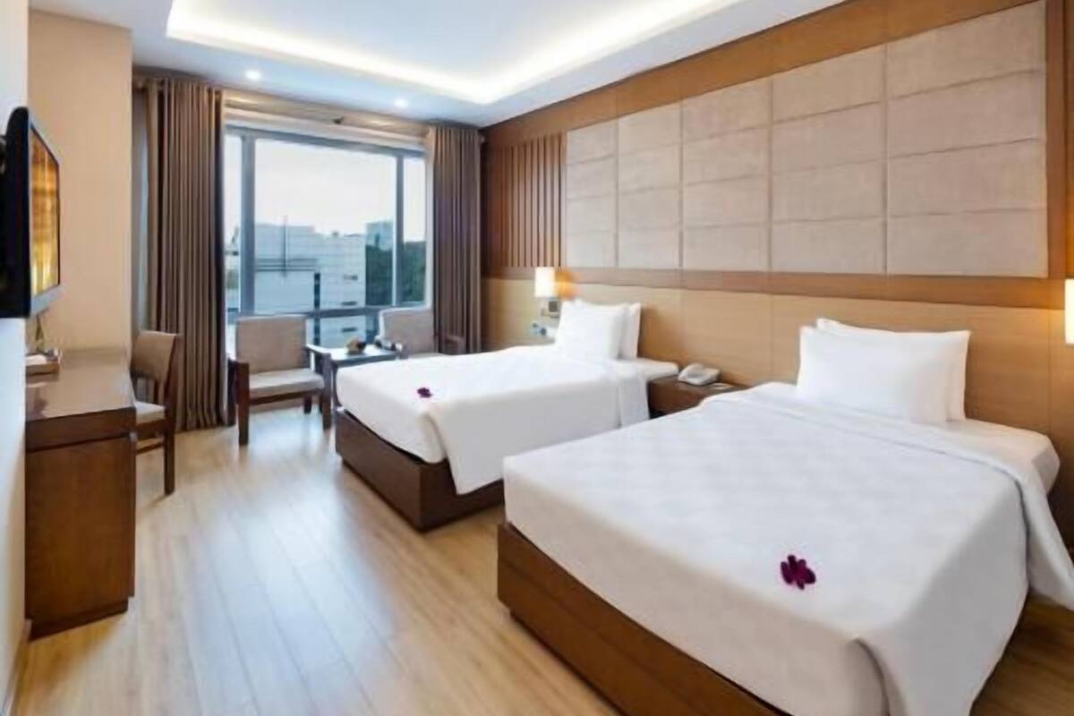 Une chambre d’hôtel avec deux lits, un bureau, une chaise et une grande fenêtre.