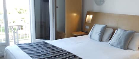 Ein Hotelzimmer mit einem großen Bett, einem Kleiderschrank, einem Nachttisch mit Lampe und einer Schiebetür zum Balkon.