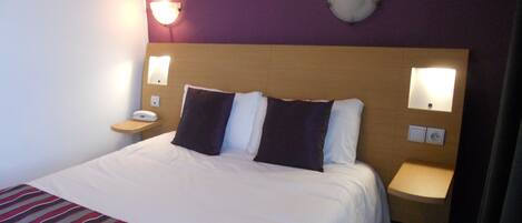 A hotel room with a large bed, two bedside tables, and wall-mounted lamps.