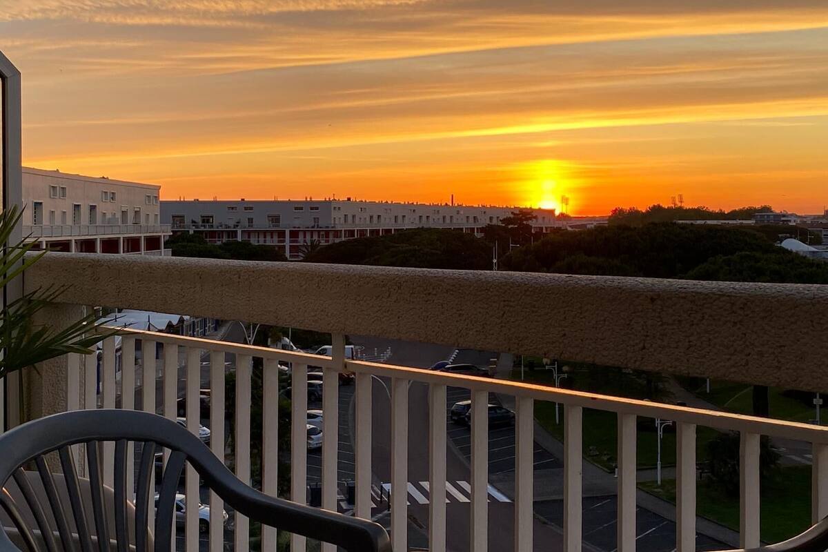 Uma varanda com vista para um pôr do sol sobre a paisagem urbana.